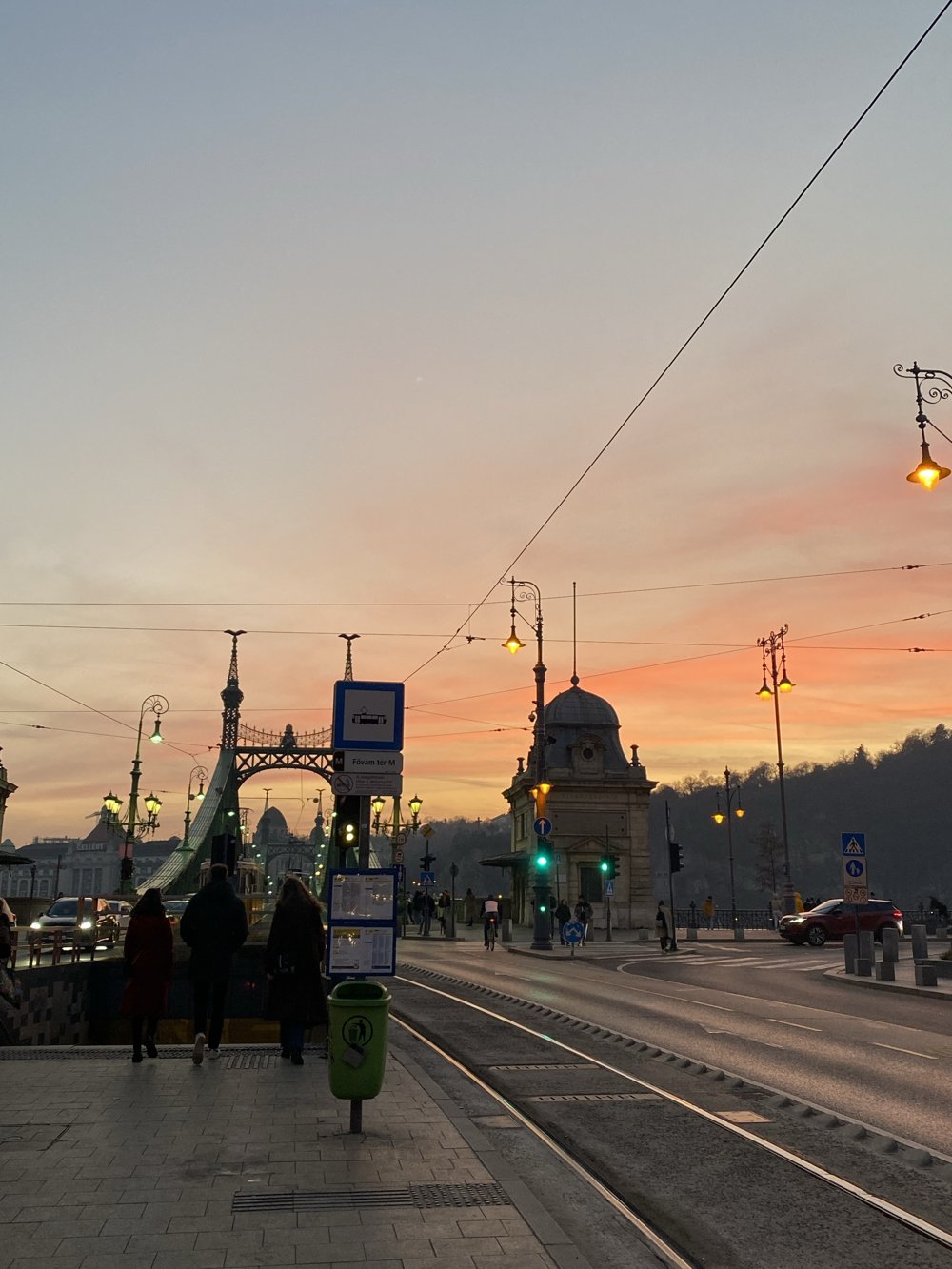 Coucher de soleil orangé sur Budapest, avec le pont de la Liberté, ses lampadaires allumés et les rails du tramway